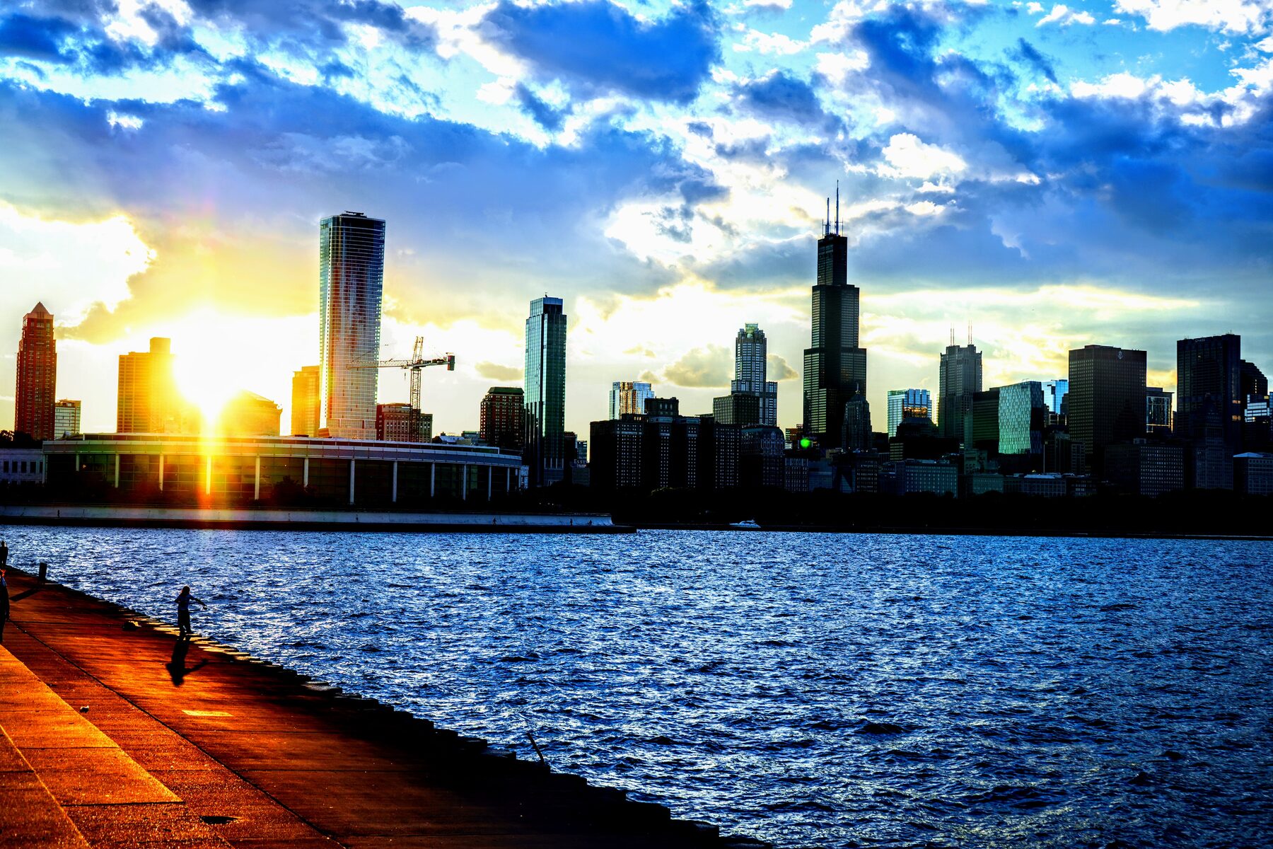 The Chicago skyline at sunset from the lakefront, with the sun flaring low between the buildings
